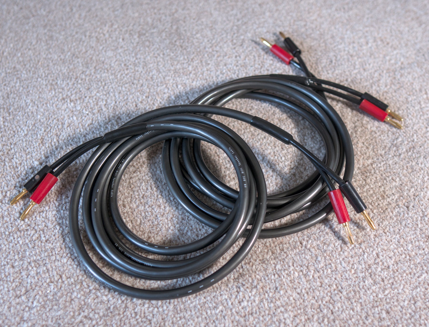 Black loudspeaker cable coil with red and gold banana plug ends, neatly looped