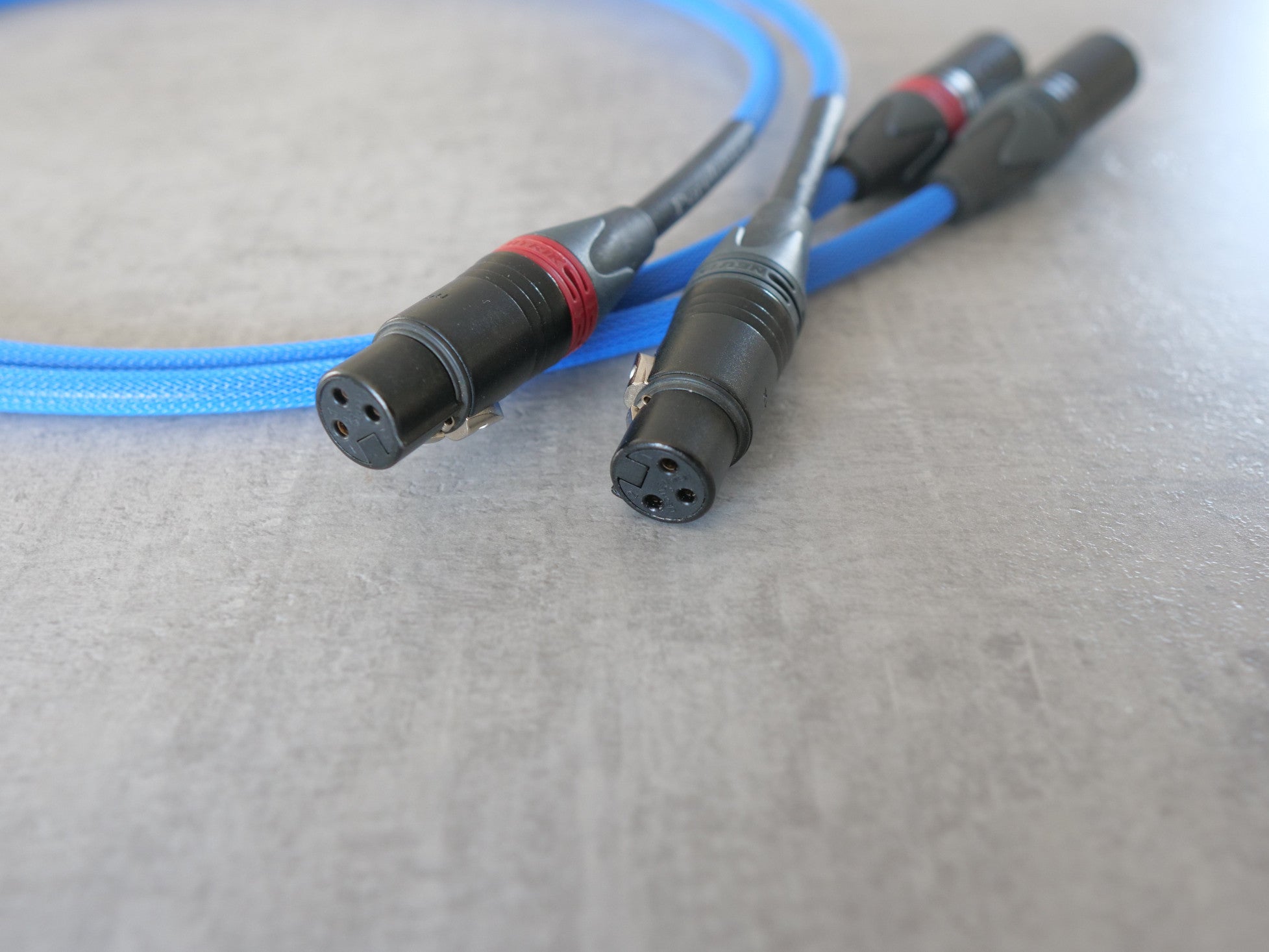 Blue XLR audio cable with four black connector pins and red rings on ends