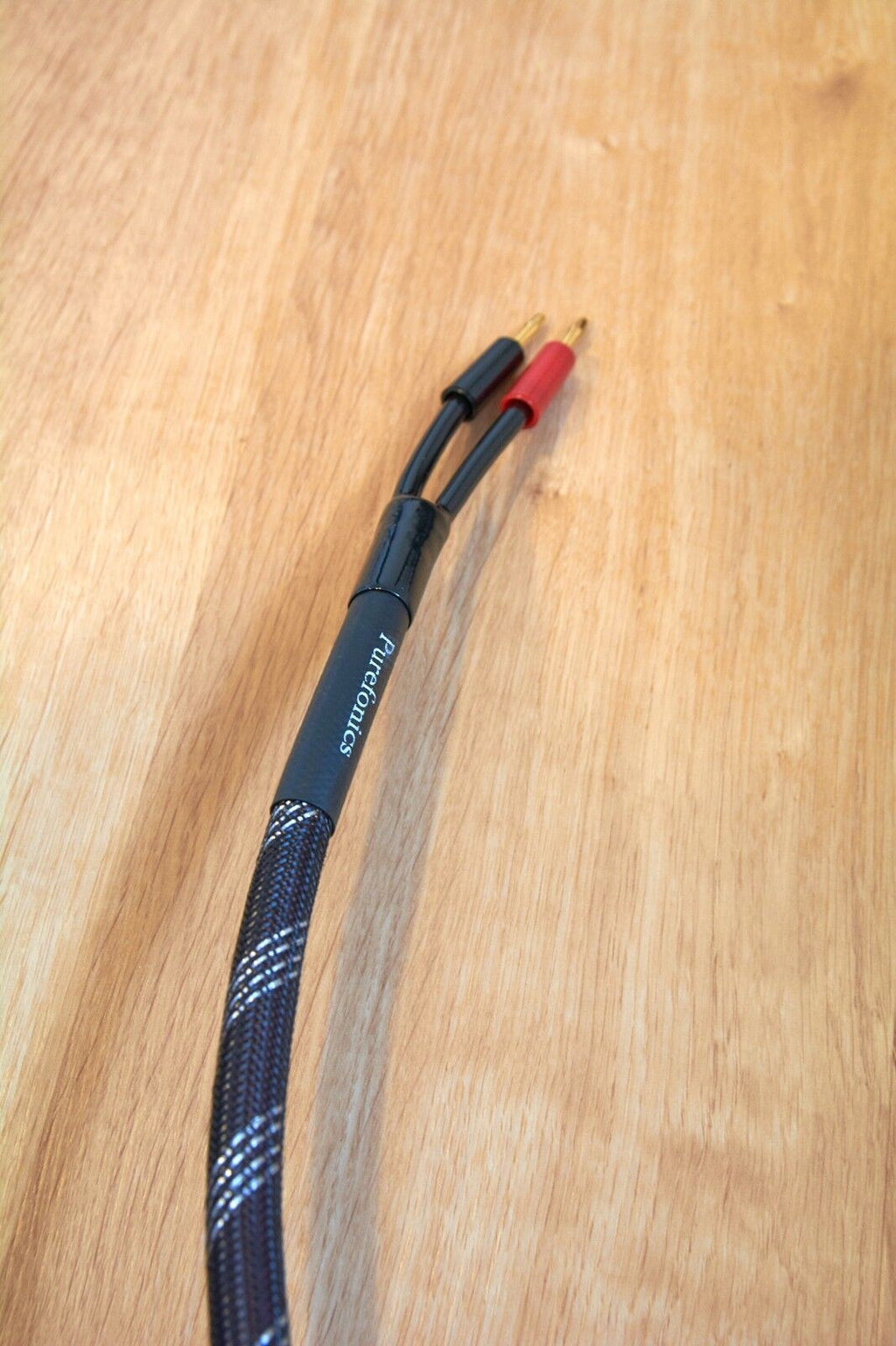 Braided black audio cable with gold banana plugs and red sleeve at connector end