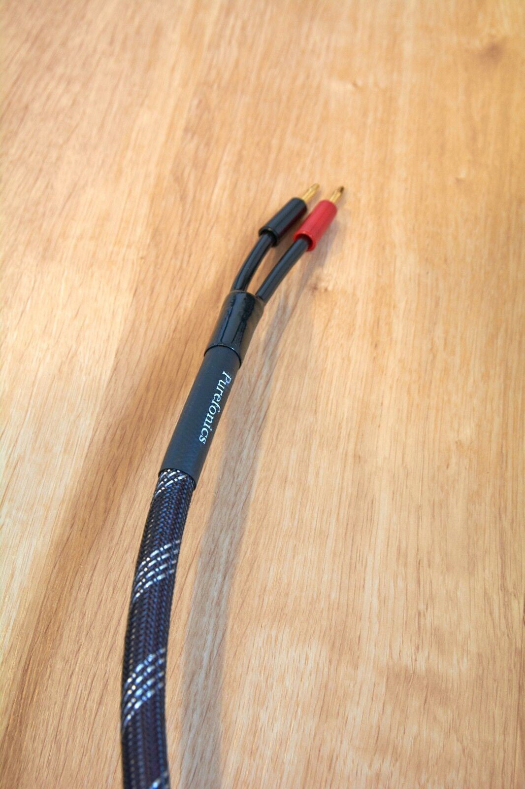 Braided black audio cable with gold banana plugs and red sleeve at connector end
