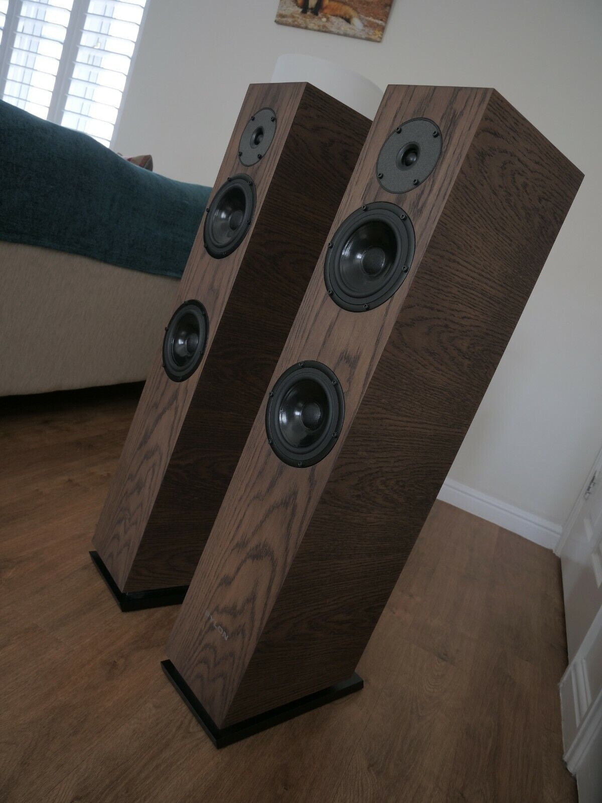Chocolate-brown floorstanding speakers on stands, angled view with multiple black driver cones