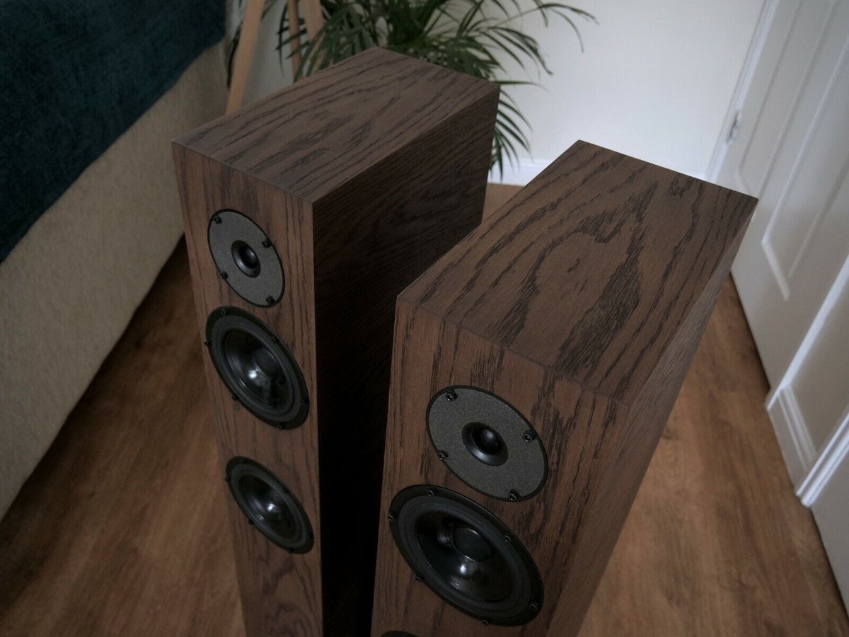 Chocolate-brown speaker pair angled view with black drivers and circular tweeter plate