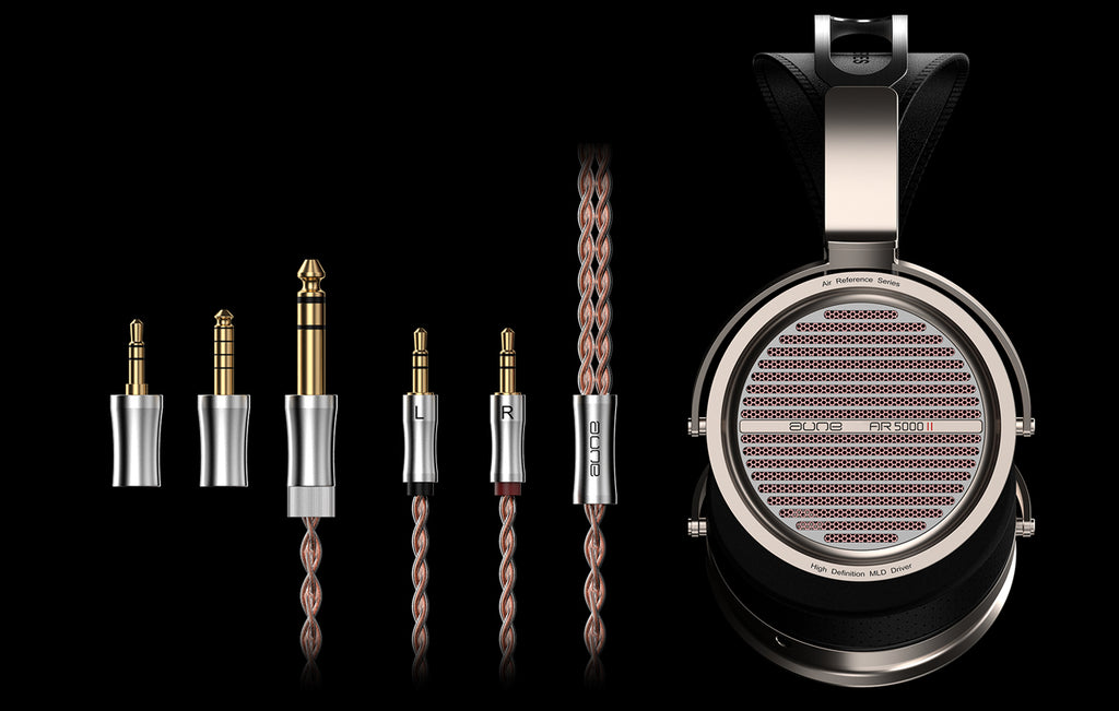 A pair of over-ear headphones with metallic silver and black housings, shown alongside five audio adapter plugs and braided copper-colored cables on a black background.