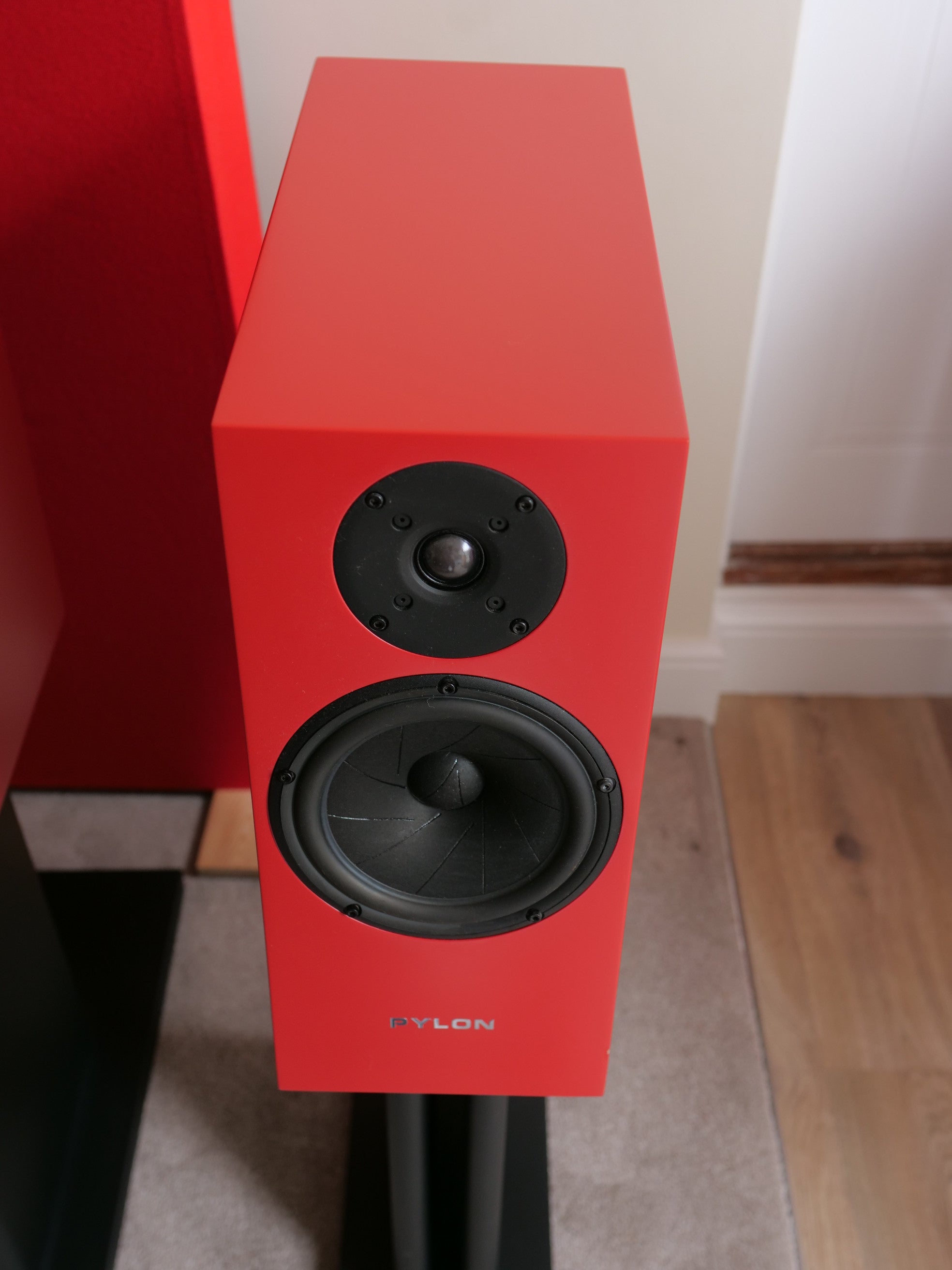 Red speaker with visible tweeter and woofer drivers on a black stand