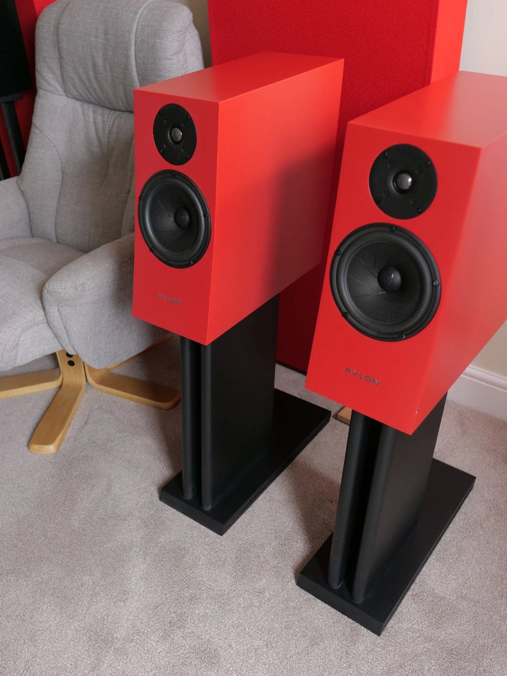 Two red floor-standing speakers with black woofers and tweeters on stands