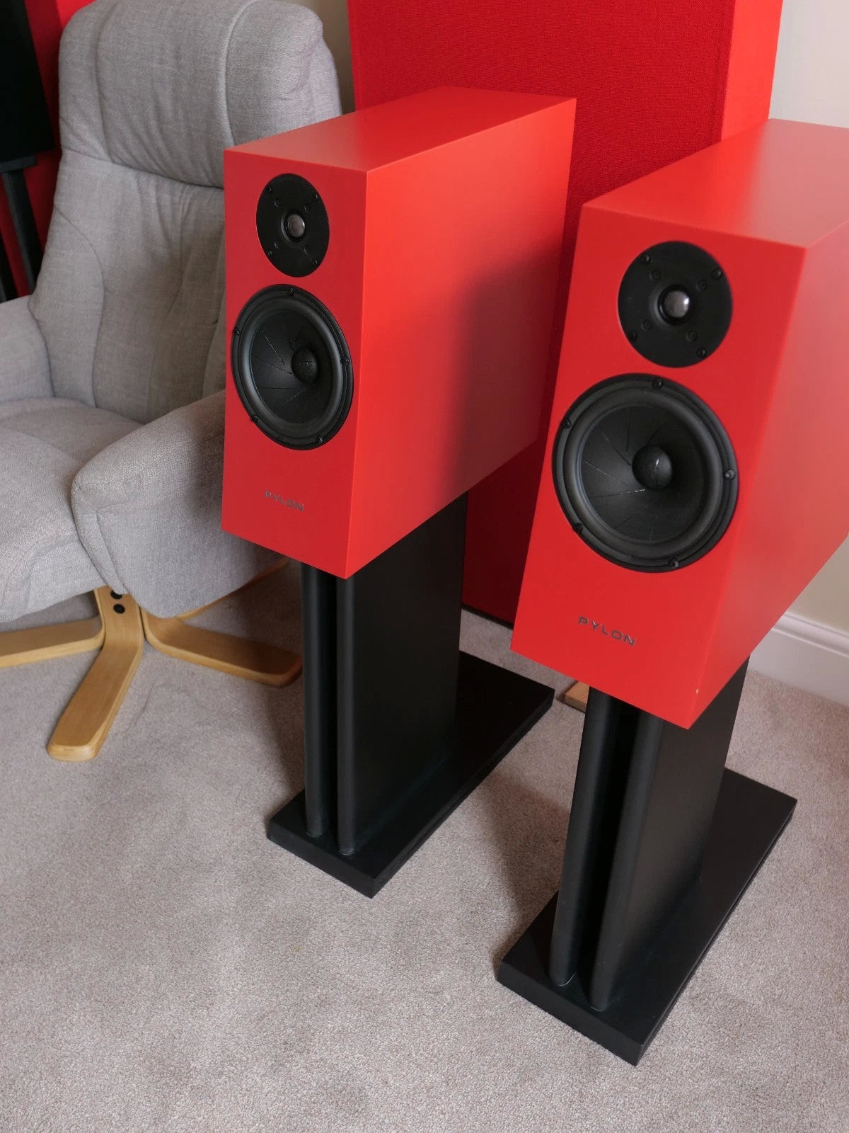 Two red floor-standing speakers with black woofers and tweeters on stands
