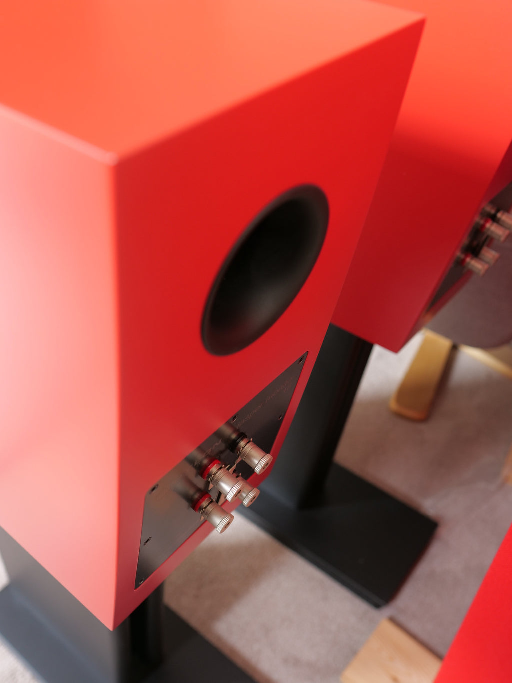 Red speaker cabinet with black woofer and exposed wiring terminals on stand