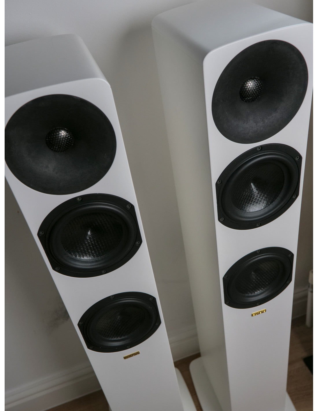 A pair of white floorstanding Aurelia Ambera II Floorstanding Loudspeakers with black drivers, standing against a neutral indoor wall.