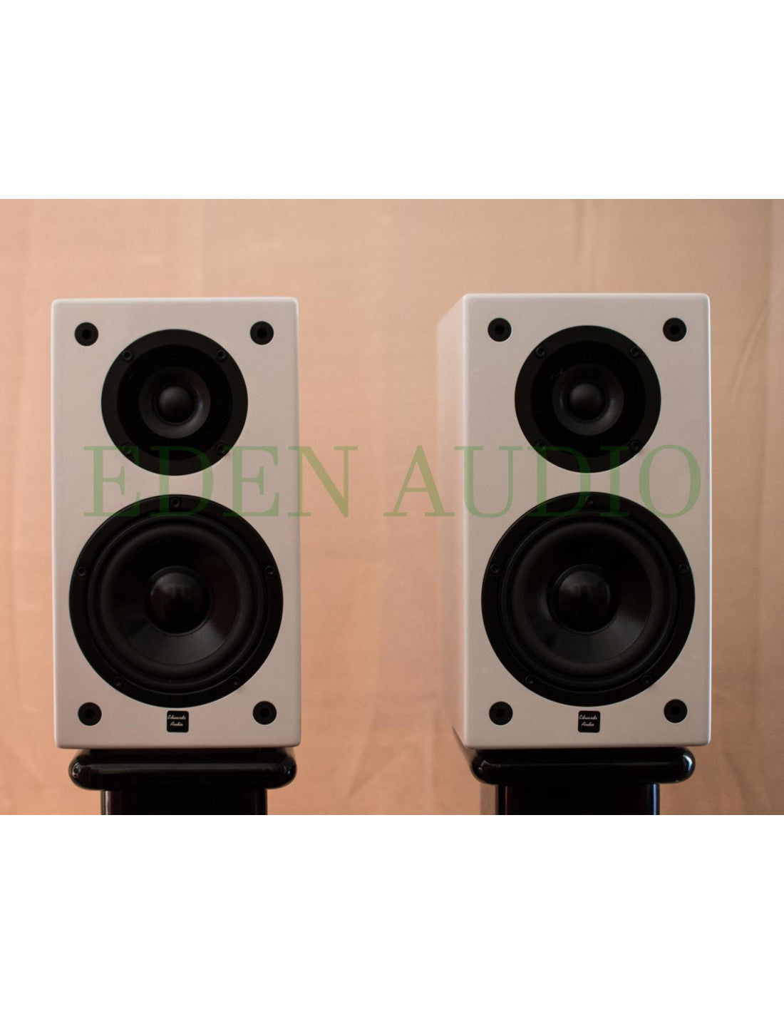 Two white Edwards Audio bookshelf speakers with black woofers, displayed side-by-side on black stands against a beige background with a green 'EDEN AUDIO' watermark.