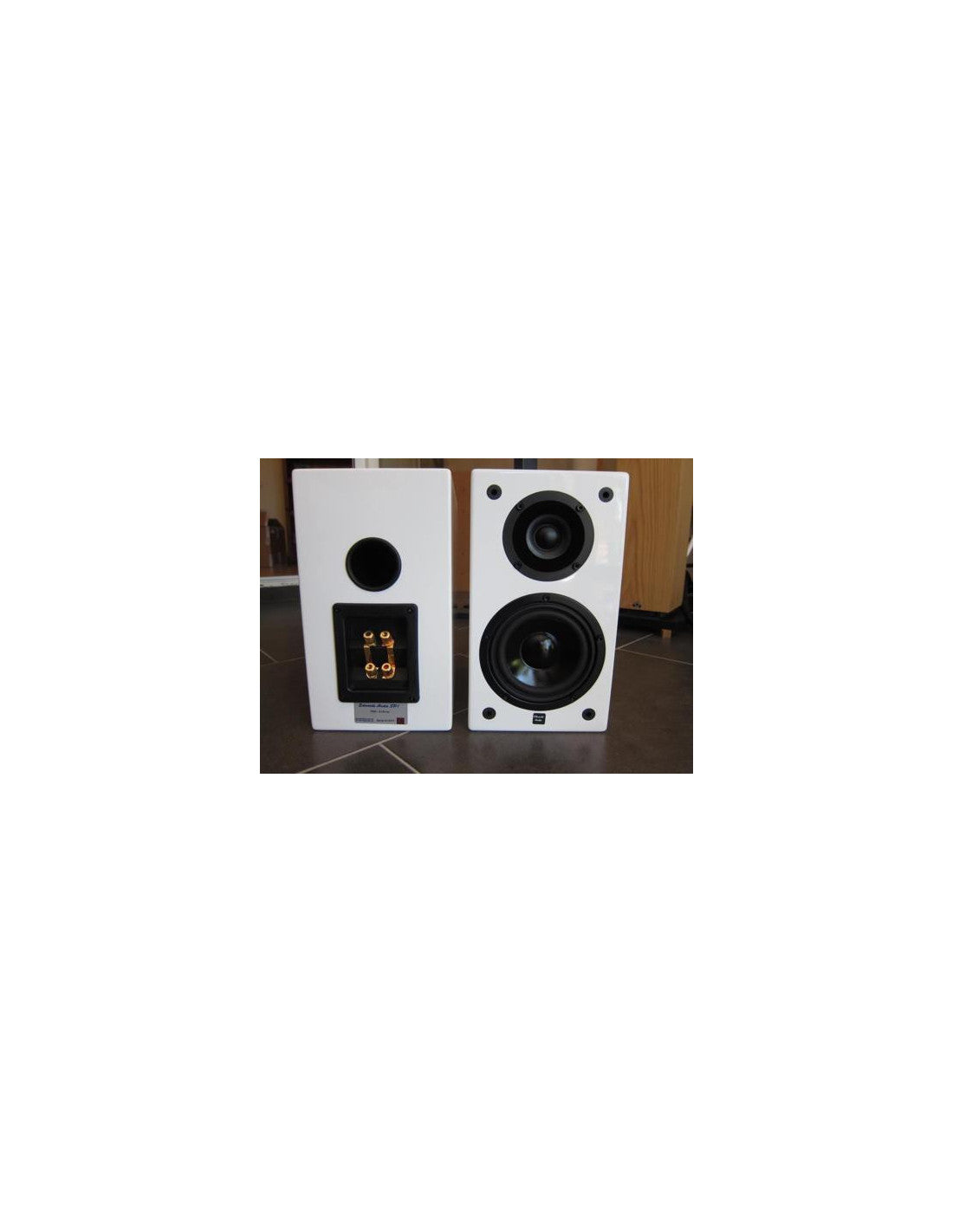 Two Edwards Audio white bookshelf speakers with black drivers, shown side-by-side on a dark floor with a wooden cabinet in the background.