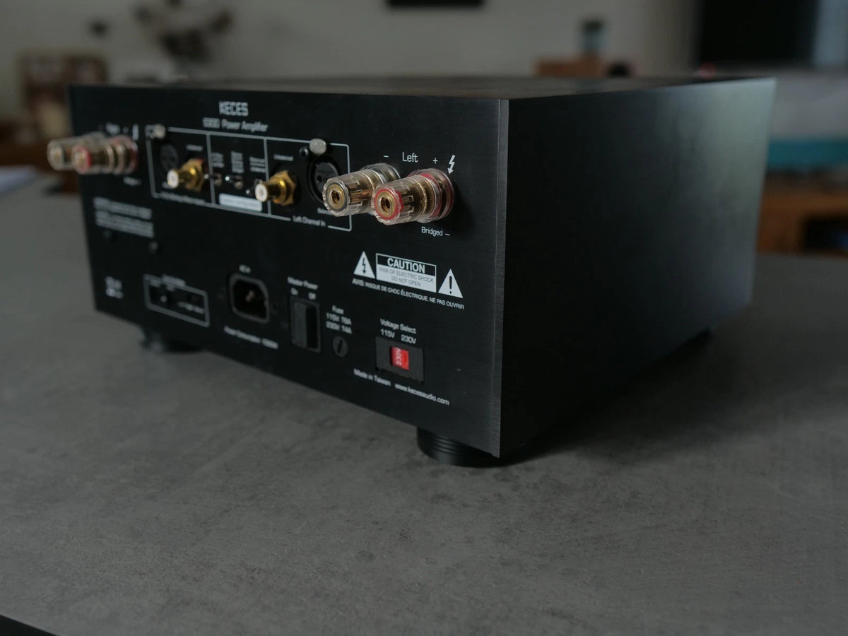 A black KECES S3000 power amplifier receiver sitting on a gray tabletop, showing the rear panel with various input and output connectors.